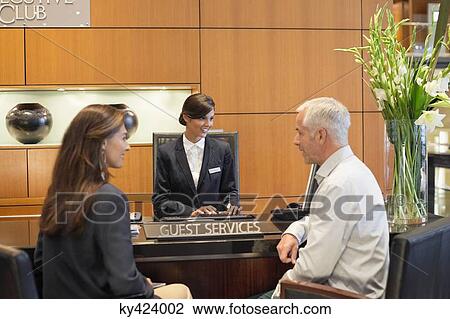 Stock Image - Business couple talking at a hotel reception counter. Fotosearch