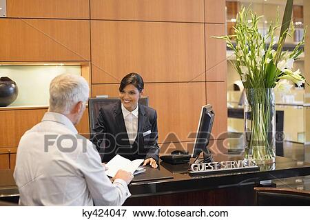 Businessman talking with a receptionist at the hotel reception counter View Large Photo Image Stock Photo - Businessman talking with a receptionist at the hotel reception counter. Fotosearch
