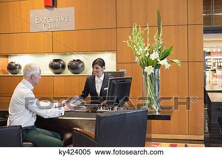 Businessman talking with a receptionist at the hotel reception counter View Large Photo Image Stock Photography - Businessman talking with a receptionist at the hotel reception counter. Fotosearch