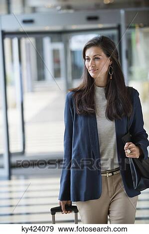 Stock Photo - Businesswoman pulling a suitcase in a hotel lobby. Fotosearch
