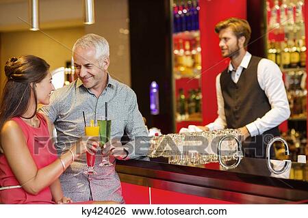 Couple enjoying drinks at the bar counter View Large Photo Image Stock Photograph - Couple enjoying drinks at the bar counter. Fotosearch