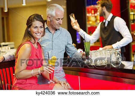 Couple enjoying drinks at the bar counter View Large Photo Image Stock Photograph - Couple enjoying drinks at the bar counter. Fotosearch