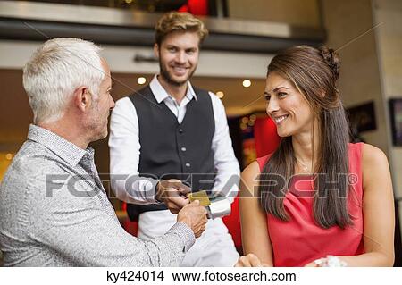 Couple paying with a credit card to a waiter in a restaurant View Large Photo Image Picture - Couple paying with a credit card to a waiter in a restaurant. Fotosearch
