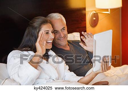 Couple video calling on a digital tablet in a hotel room View Large Photo Image Stock Photography - Couple video calling on a digital tablet in a hotel room. Fotosearch