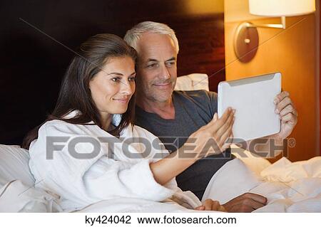 Couple watching movie on a digital tablet in a hotel room View Large Photo Image Stock Image - Couple watching movie on a digital tablet in a hotel room. Fotosearch
