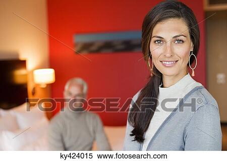 Portrait of a woman smiling in a hotel room with her husband in the background View Large Photo Image Stock Photography - Portrait of a woman smiling in a hotel room with her husband in the background. Fotosearch