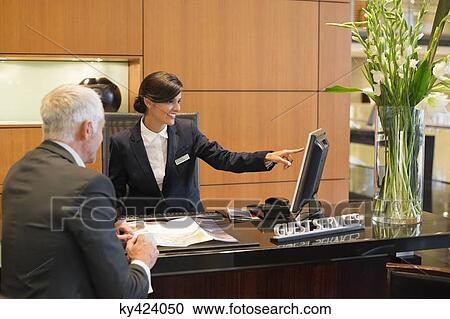 Receptionist pointing on a desktop pc with a businessman at the hotel reception counter View Large Photo Image Stock Image - Receptionist pointing on a desktop pc with a businessman at the hotel reception counter. Fotosearch