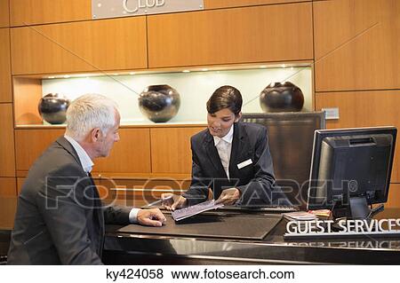 Receptionist showing a brochure to a businessman at a hotel reception counter View Large Photo Image Stock Photo - Receptionist showing a brochure to a businessman at a hotel reception counter. Fotosearch