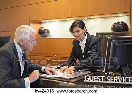 Stock Photograph - Receptionist showing a brochure to a businessman at a hotel reception counter. Fotosearch