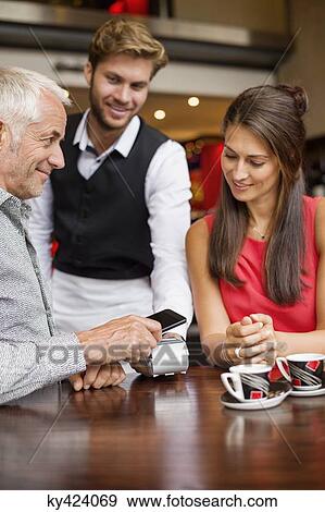 Stock Photo - Waiter showing credit card reader to a couple on a table in a restaurant. Fotosearch
