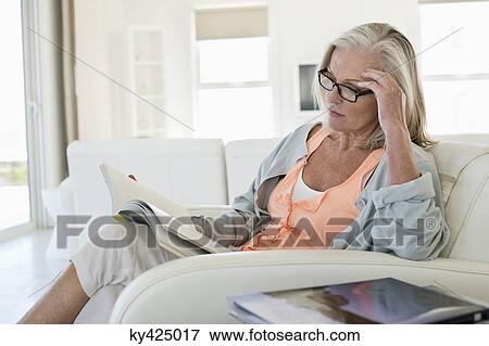 Stock Photo - Woman sitting on a couch and reading a book at home. Fotosearch