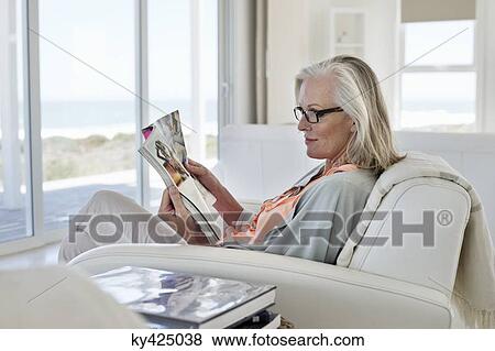 Woman sitting on a couch and reading a magazine at home View Large Photo Image Stock Photo - Woman sitting on a couch and reading a magazine at home. Fotosearch