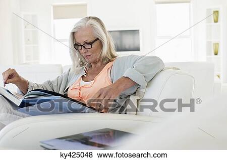 Stock Photo - Woman sitting on a couch and reading a book at home. Fotosearch