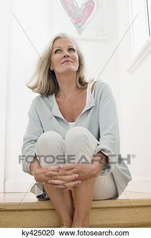 Stock Image - Woman sitting on a table and looking up. Fotosearch