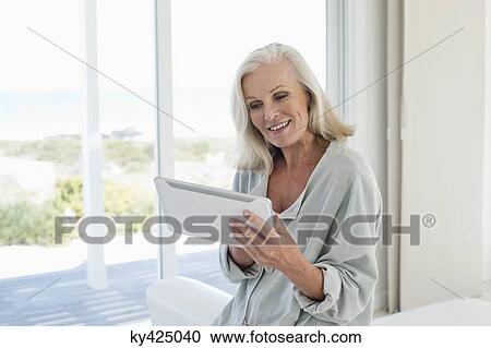 Woman using a digital tablet and smiling at home View Large Photo Image Stock Image - Woman using a digital tablet and smiling at home. Fotosearch