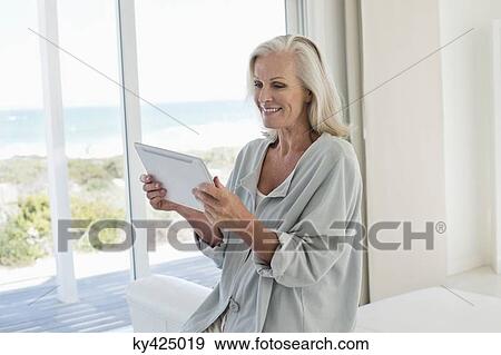 Woman using a digital tablet and smiling at home View Large Photo Image Stock Photo - Woman using a digital tablet and smiling at home. Fotosearch