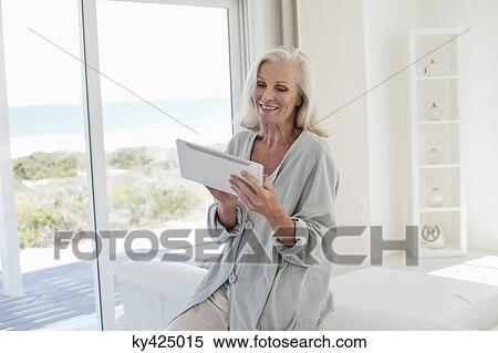 Stock Photography - Woman using a digital tablet and smiling at home. Fotosearch
