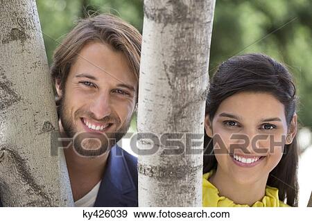 Portrait of a couple smiling behind a tree View Large Photo Image Stock Photo - Portrait of a couple smiling behind a tree. Fotosearch