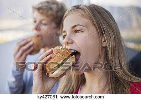Stock Image - Close-up of two friends eating hamburger. Fotosearch
