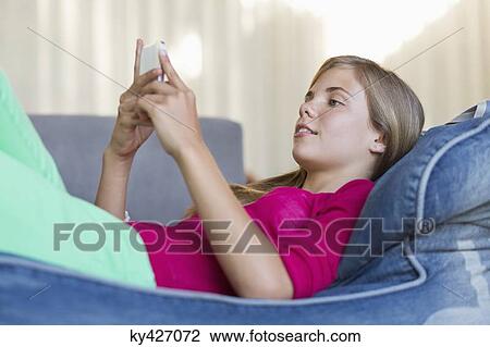 Girl lying on a bean bag and using a mobile phone View Large Photo Image Stock Image - Girl lying on a bean bag and using a mobile phone. Fotosearch