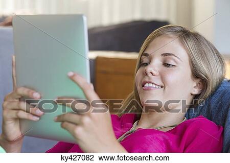 Stock Image - Girl lying on a bean bag and using a digital tablet. Fotosearch