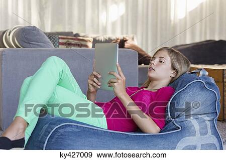 Stock Photo - Girl lying on a bean bag and using a digital tablet. Fotosearch
