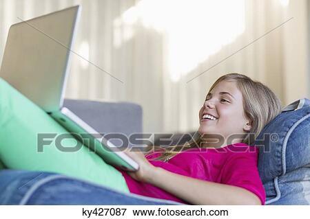 Girl lying on a bean bag and using a laptop View Large Photo Image Stock Photo - Girl lying on a bean bag and using a laptop. Fotosearch