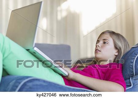 Girl lying on a bean bag and using a laptop View Large Photo Image Stock Photograph - Girl lying on a bean bag and using a laptop. Fotosearch