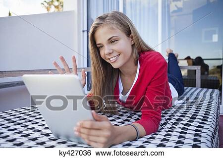 Girl lying on the bed and video chatting on a digital tablet View Large Photo Image Stock Photograph - Girl lying on the bed and video chatting on a digital tablet. Fotosearch