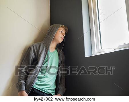 Stock Image - Teenage boy leaning against a wall and thinking. Fotosearch