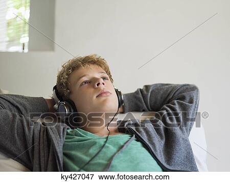 Stock Photo - Teenage boy lying on the bed and listening to music. Fotosearch