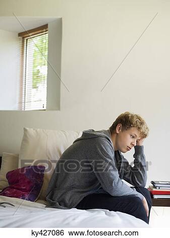 Stock Photograph - Teenage boy sitting on the bed and thinking. Fotosearch