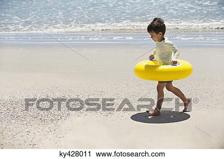 Stock Image - Boy holding an inflatable ring and walking on the beach. Fotosearch