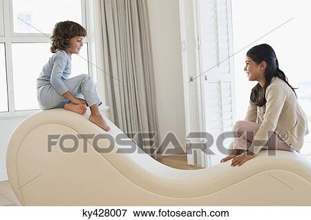 Stock Photo - Brother and his sister sitting at the edges of a chaise longue. Fotosearch