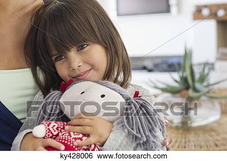 Stock Photograph - Close-up of a girl sitting with her mother and holding a rag doll. Fotosearch