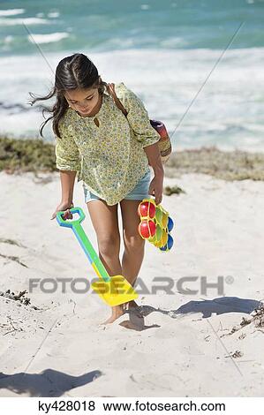 Stock Photo - Girl carrying shovel and toy on the beach. Fotosearch
