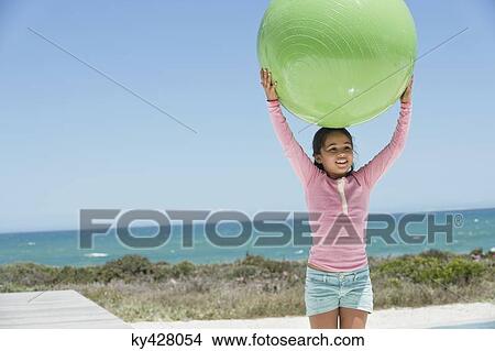 Picture - Girl holding a fitness ball on the beach. Fotosearch