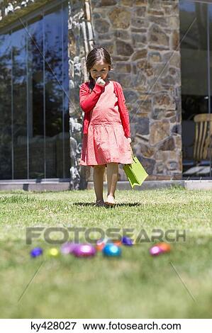 Girl looking at Easter eggs in a lawn View Large Photo Image Stock Photo - Girl looking at Easter eggs in a lawn. Fotosearch