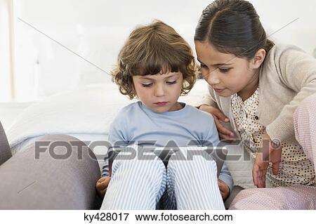 Girl looking at her brother using a digital tablet View Large Photo Image Stock Photo - Girl looking at her brother using a digital tablet. Fotosearch