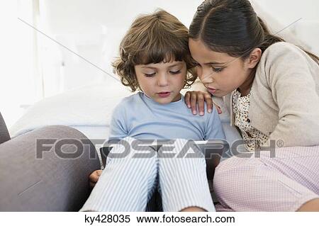 Girl looking at her brother using a digital tablet View Large Photo Image Stock Photography - Girl looking at her brother using a digital tablet. Fotosearch