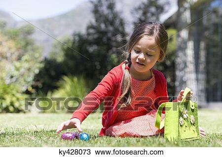 Stock Image - Girl picking up Easter eggs in a lawn. Fotosearch
