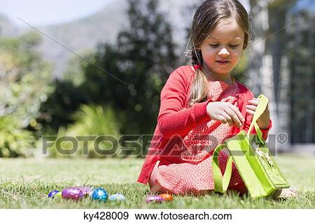 Girl picking up Easter eggs in a lawn View Large Photo Image Stock Photo - Girl picking up Easter eggs in a lawn. Fotosearch