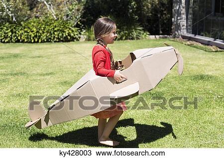Stock Image - Girl playing with a cardboard airplane in lawn. Fotosearch