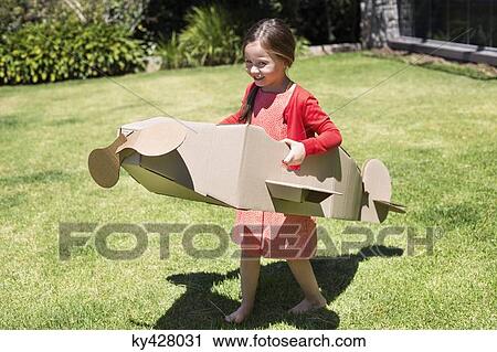 Stock Image - Girl playing with a cardboard airplane in lawn. Fotosearch