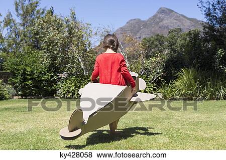 Stock Photo - Girl playing with a cardboard airplane in lawn. Fotosearch