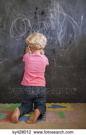 Stock Image - Rear view of a girl writing on a blackboard. Fotosearch