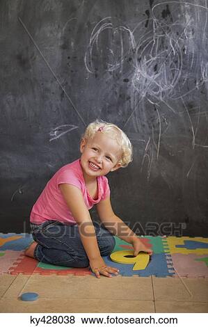 Smiling girl playing with number puzzle in front of a blackboard View Large Photo Image Stock Photo - Smiling girl playing with number puzzle in front of a blackboard. Fotosearch