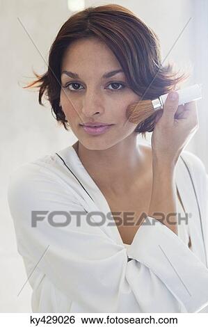Stock Photograph - Woman applying make-up on her face. Fotosearch