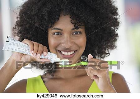 Stock Photograph - Woman squeezing out toothpaste on a toothbrush. Fotosearch