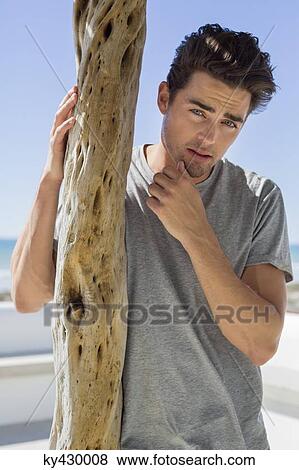 Stock Photo - Man standing beside a wooden post. Fotosearch